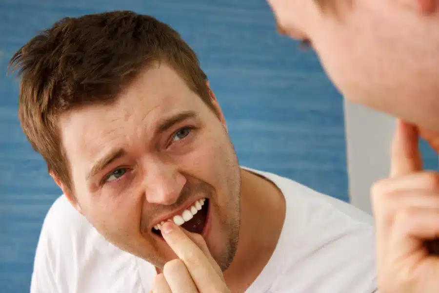 Man checking his front tooth with his finger while looking at it in a mirror